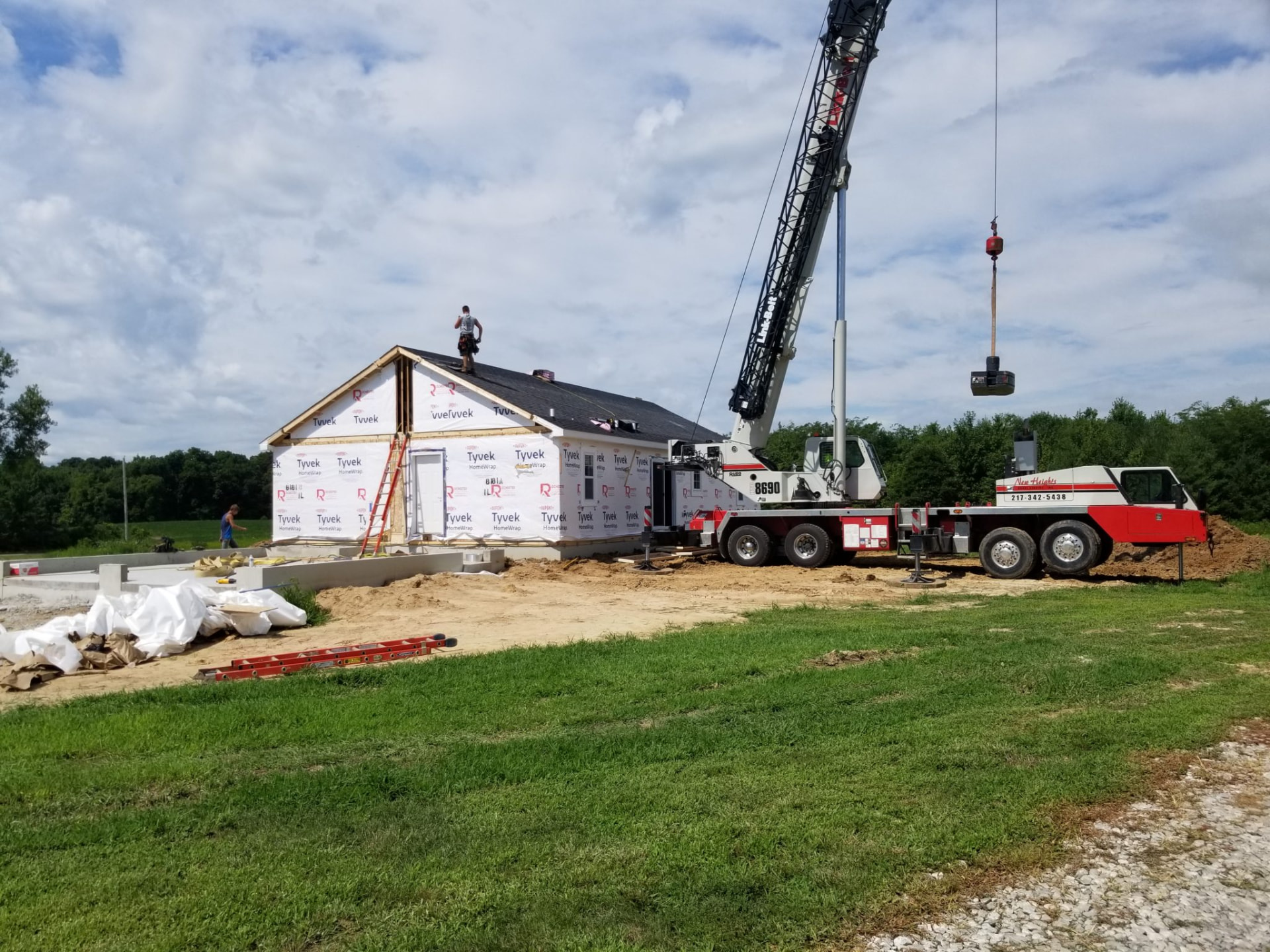 Crane truck setting a new house section onto its foundation on a rural lot