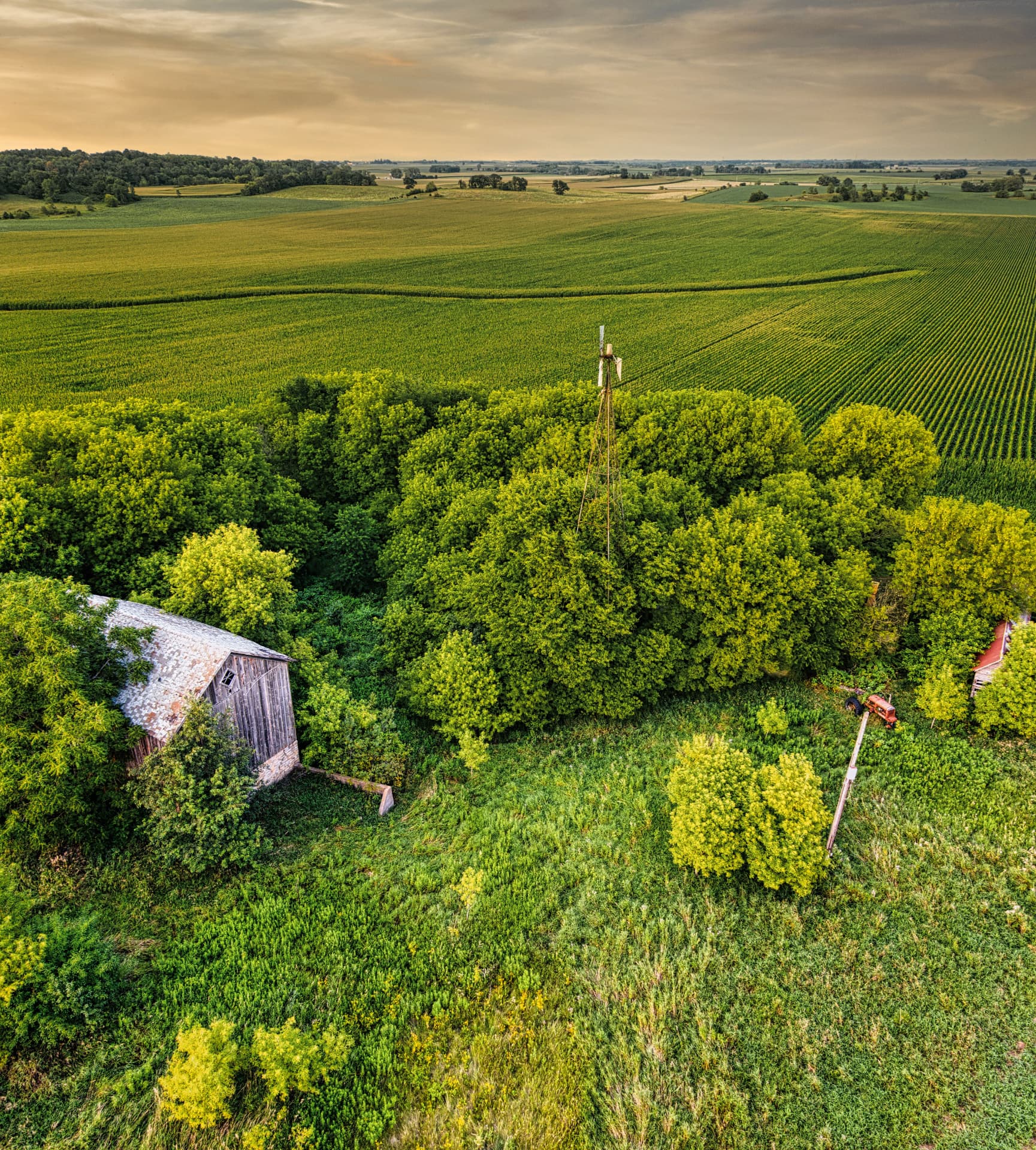 Aerial view of rolling farmland and forest with a weathered barn at dusk