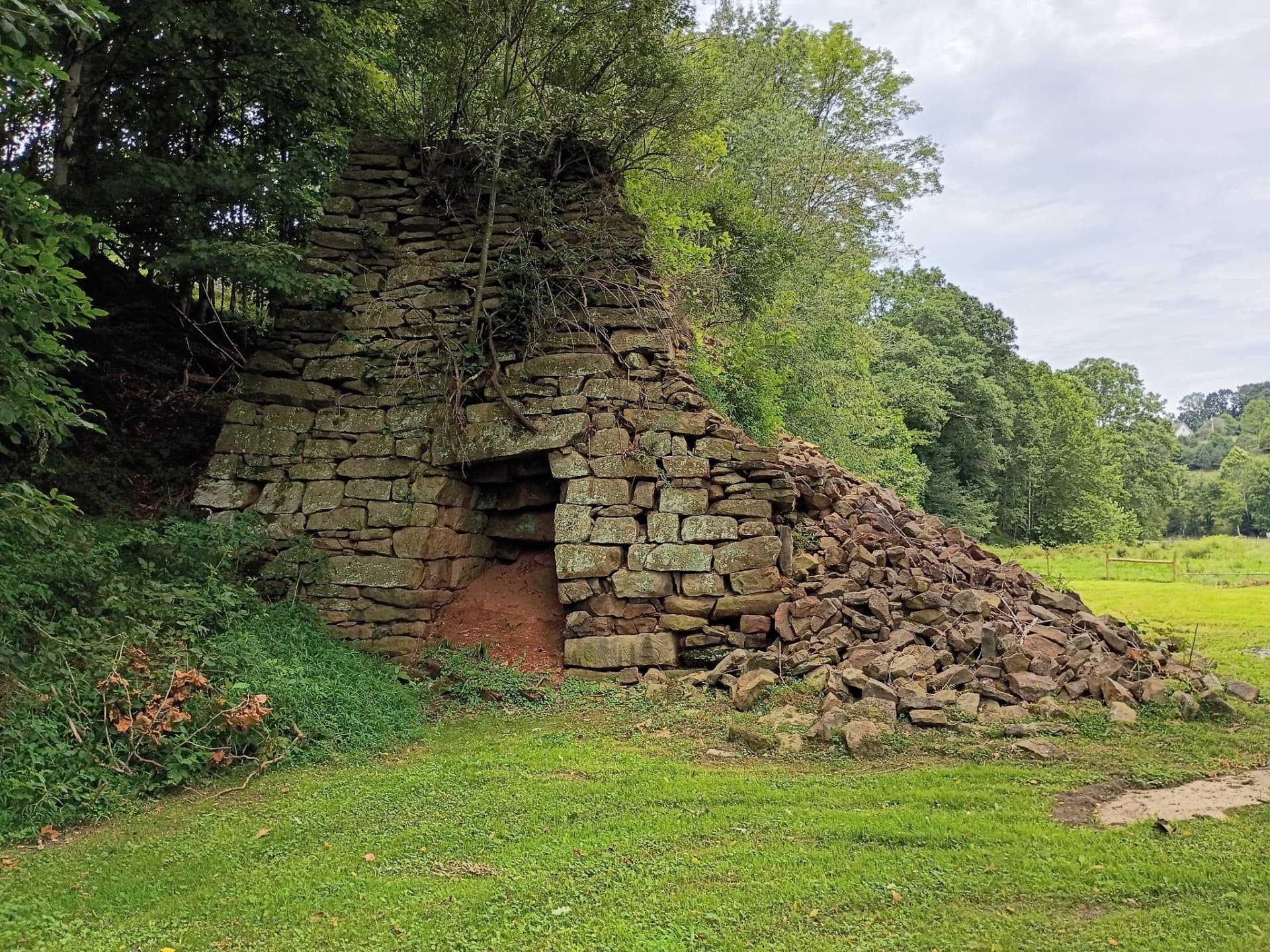 Historic stone iron furnace ruin surrounded by green pasture and trees